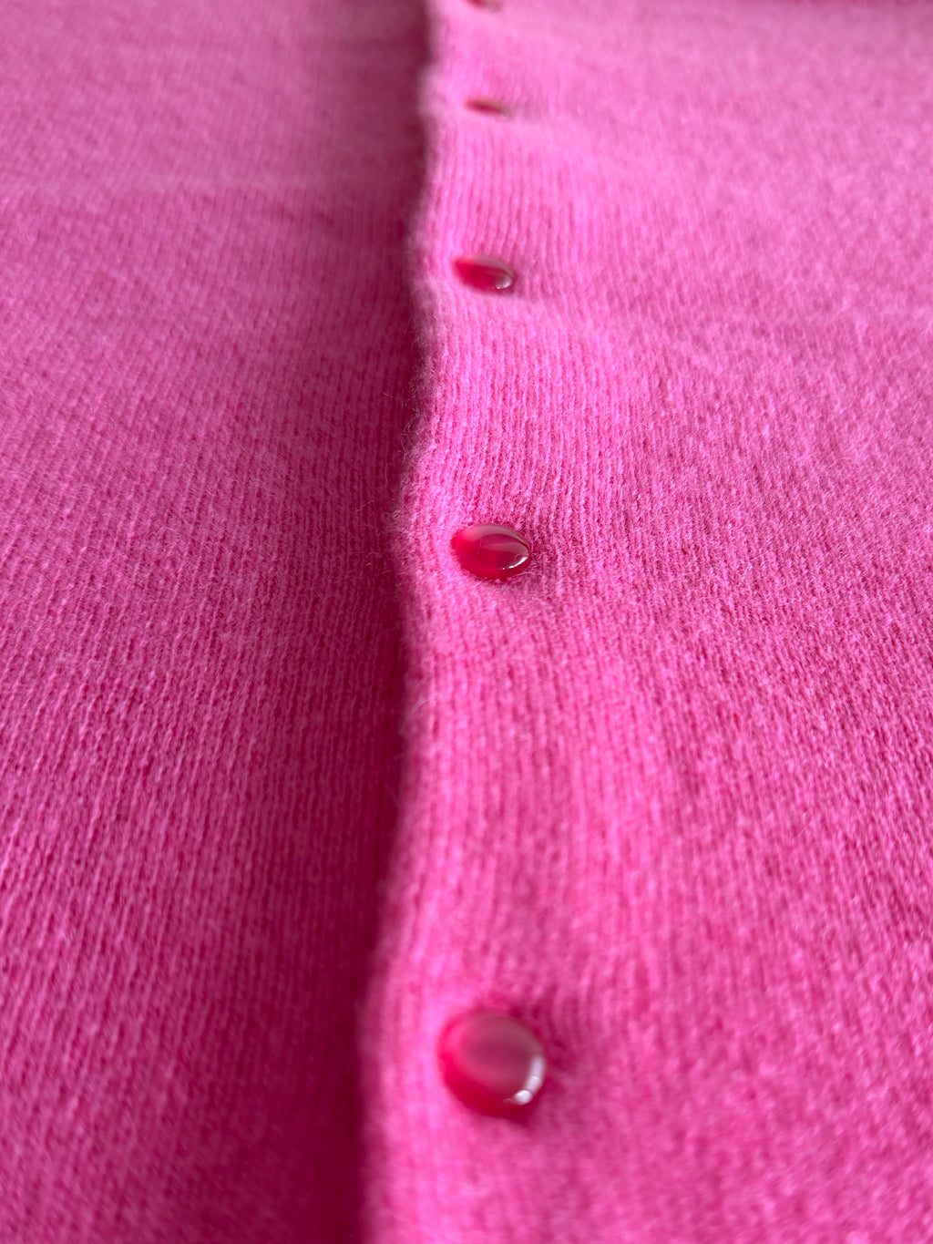 Close-up of a bright pink knit cardigan with glossy red buttons, showing the fine knit texture and glossy shank buttons.