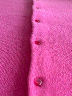 Close-up of a bright pink knit cardigan with glossy red buttons, showing the fine knit texture and glossy shank buttons.